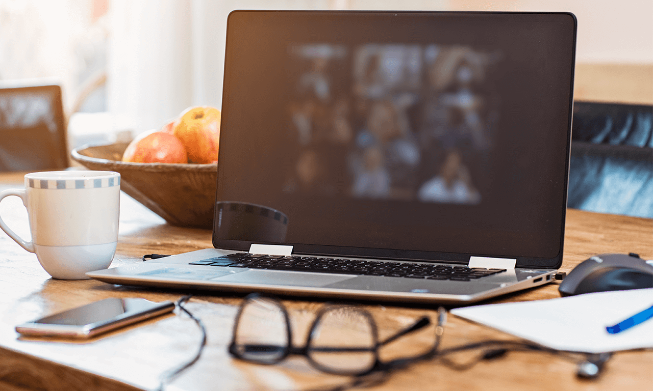 Laptop on a desk with a coffee mug, glasses and pen and paper