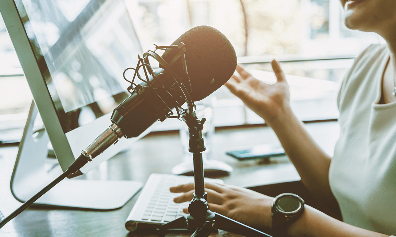 Click on the image to view podcasts; Woman on a podcast speaking into microphone.