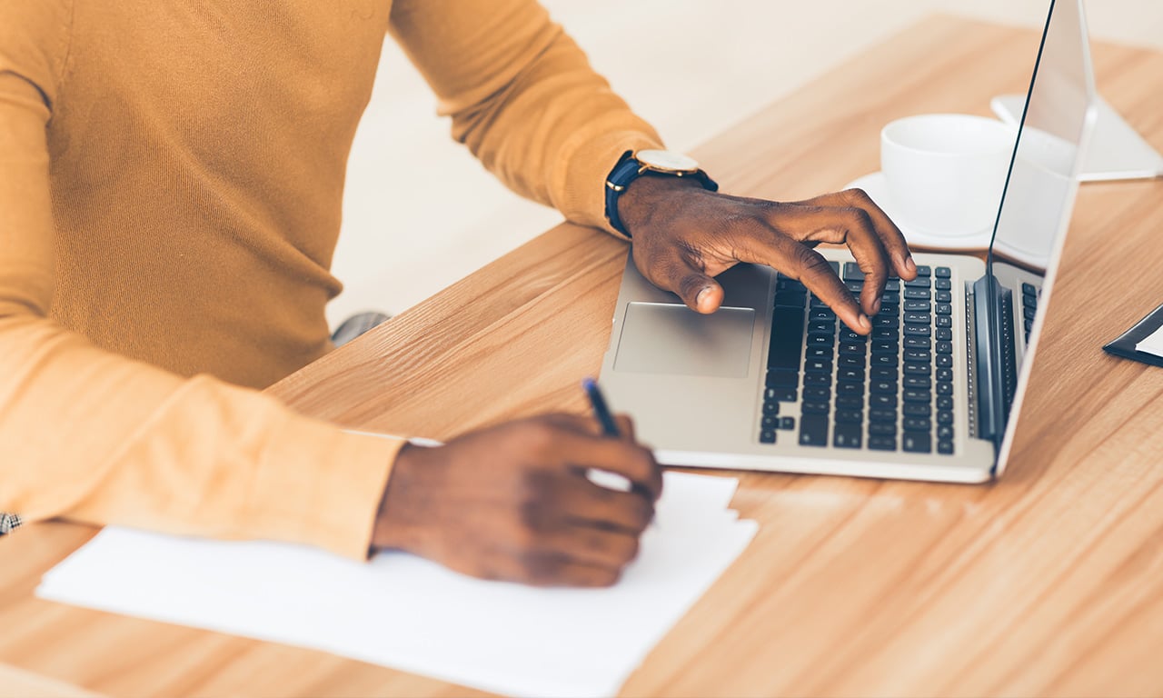 Man typing on laptop checking off a list